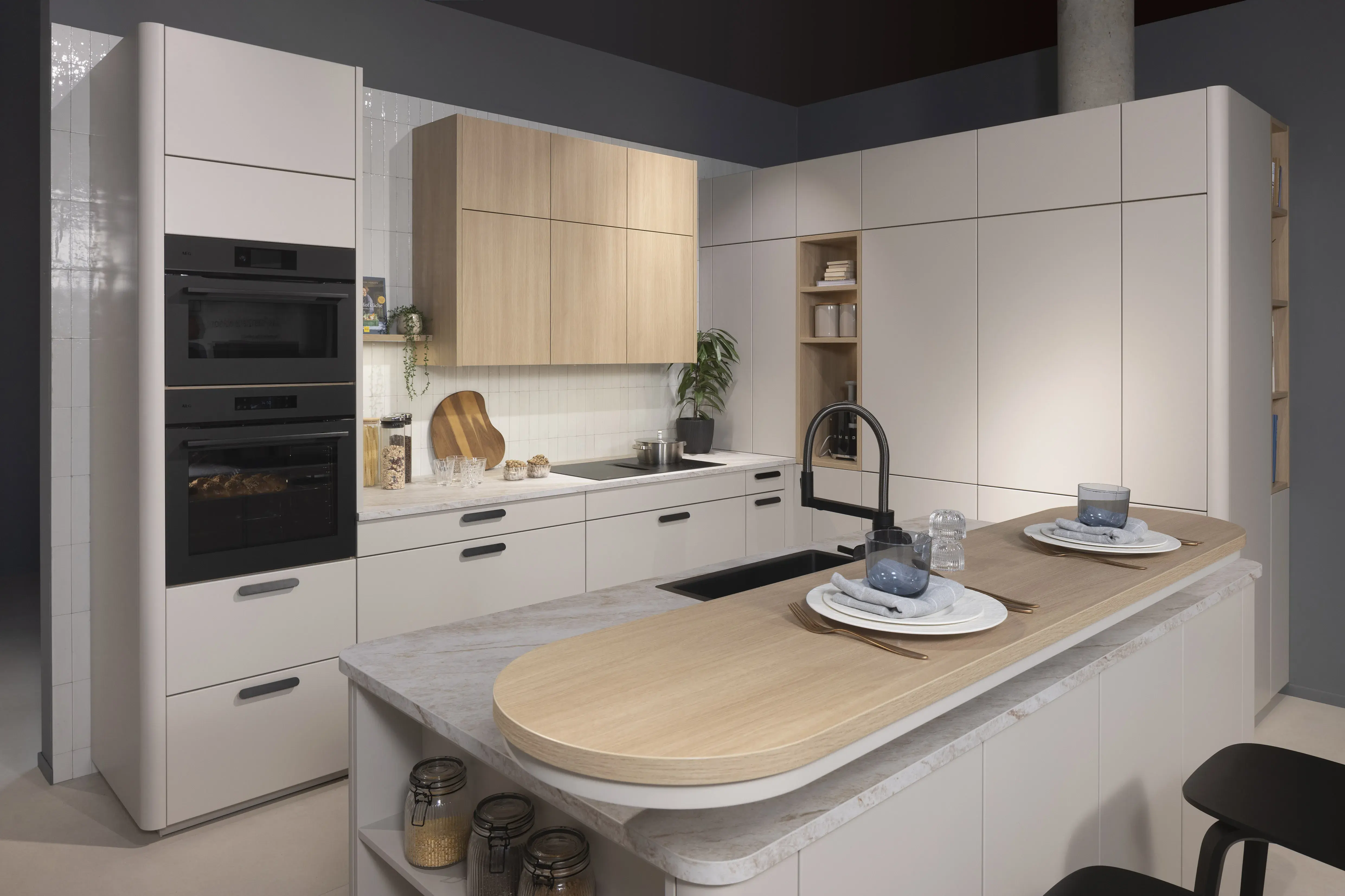 Moderne Küche mit heller Kochinsel, zwei Gedecken, schwarzen Geräten und Holzdetails.