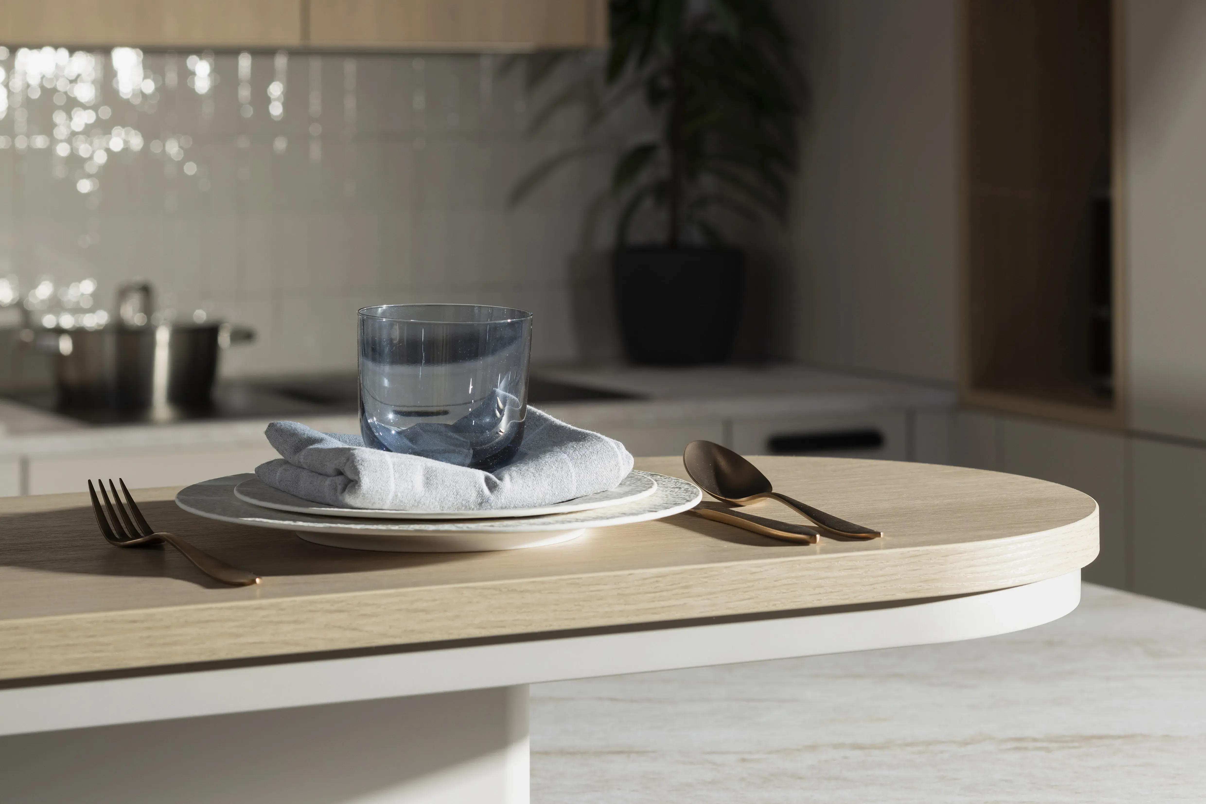 Gedeckter Frühstückstisch mit Teller, Besteck, Stoffserviette und Glas im Sonnenlicht.